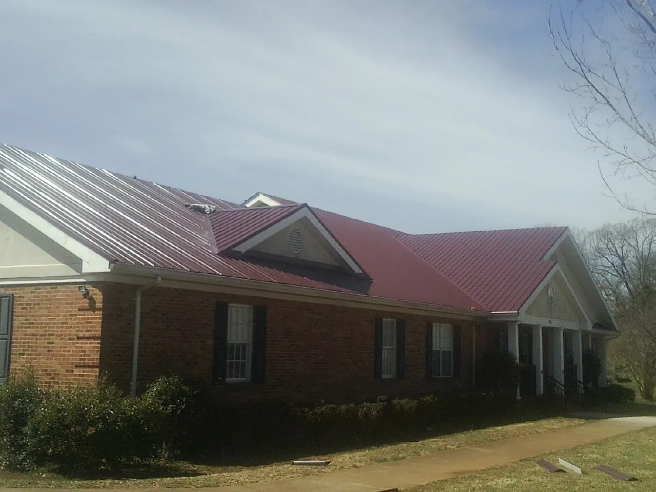 Red metal roof with gabled entries on a long brick building, from a Hail Damage Roof Repair job in Oswego