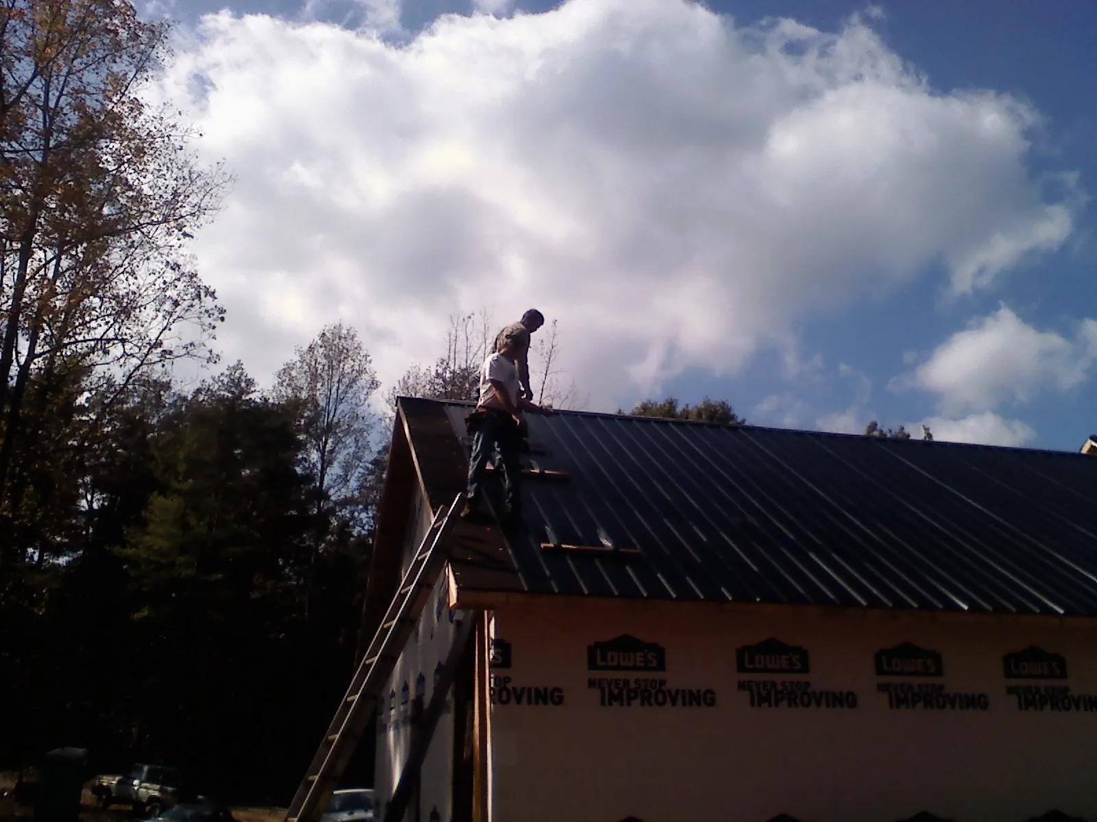 Roofer fastening dark metal panels high against a cloudy sky, from a Roof Inspection job in Oswego